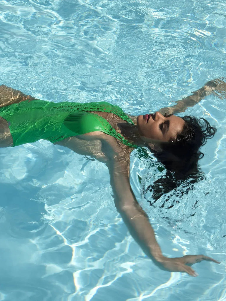 Model swimming in pool wearing green 'Ajourage Couture' swimsuit by Lise Charmel.