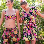 Two models, one wearing 'La Feminissima' Beach Coverup in Rose Améthyste (Floral on Black), by Antigel.