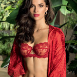 Beautiful female model wearing gorgeous red bra and red silk gown against a backdrop of tropical greenery.