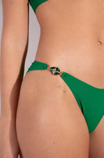 Model wearing 'Chan/Carli' Jade Halterneck Triangle Bikini Set, by Pain de Sucre (front view, focus on jewel on hip).